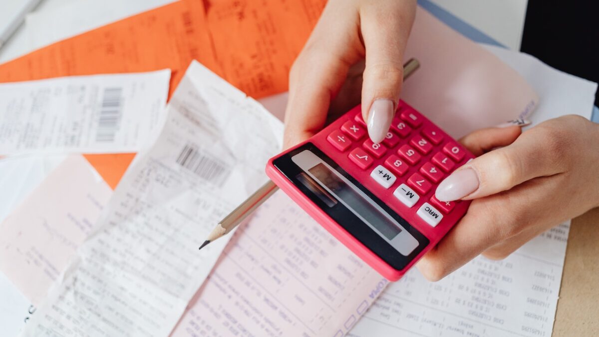 kobieta z różowym kalkulatorem w dłoniach stara się przygotować księgę przychodów i rozchodów na podstawie leżących na blacie dokumentów