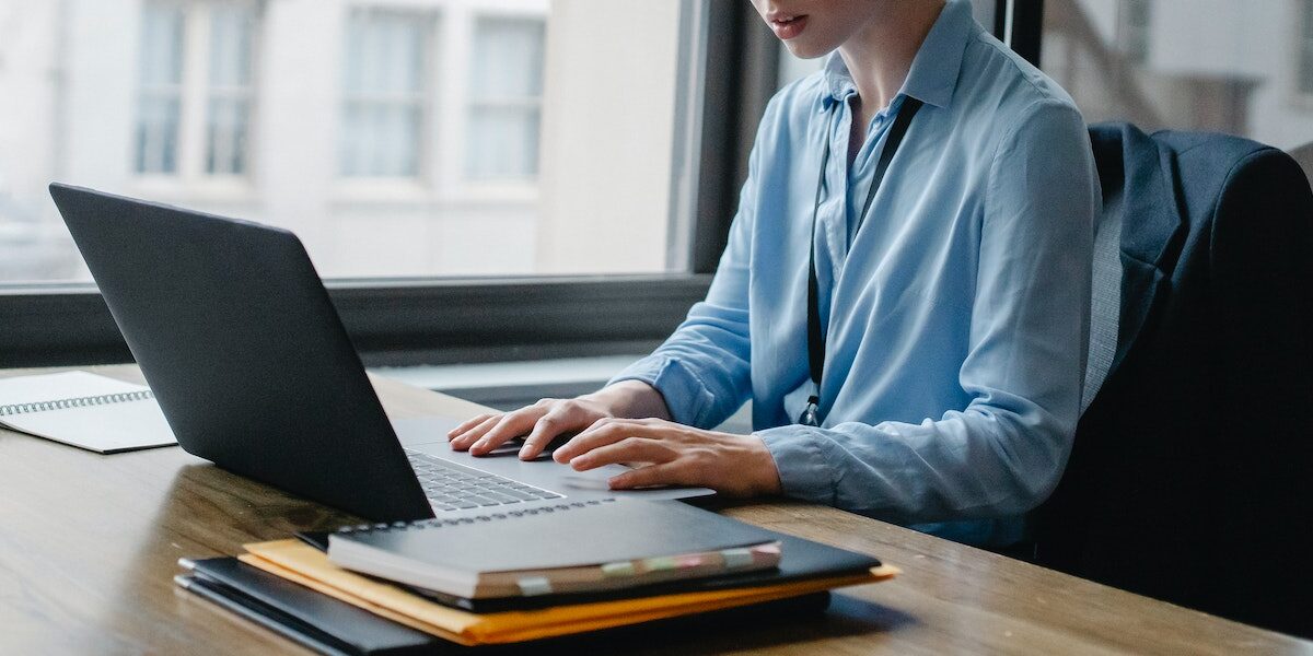 kobieta w niebieskiej koszuli siedząca przy laptopie i wystawiająca fakturę przez krajowy system e-faktur