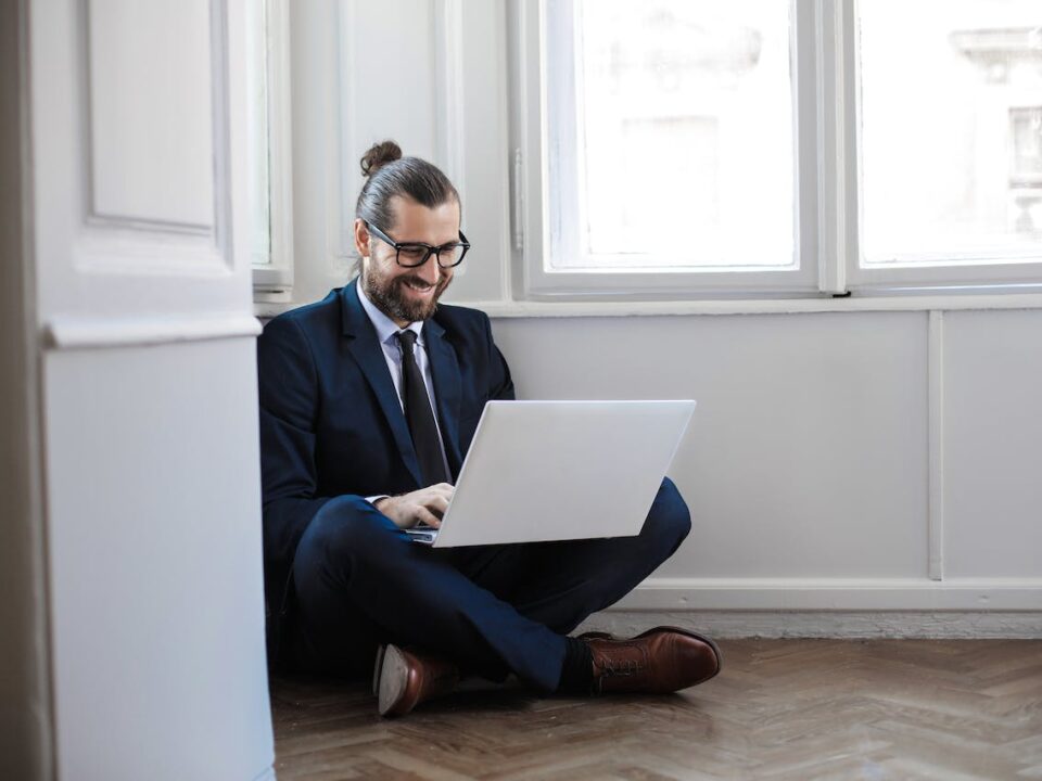 mężczyzna w garniturze siedzący na podłodze i odbierający na laptopie e-doręczenia