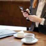kobieta siedząca przy stoliku w kawiarni i sprawdzająca w smartfonie e-paragon