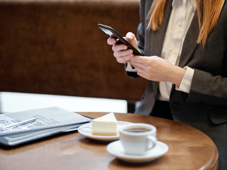 kobieta siedząca przy stoliku w kawiarni i sprawdzająca w smartfonie e-paragon